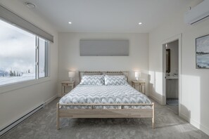 A bedroom with a large window, a bed with patterned bedding, bedside lamps, and a view of a snowy landscape.