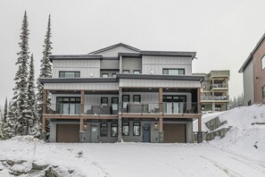 A multi-story building with a garage, balconies, and a snow-covered landscape.