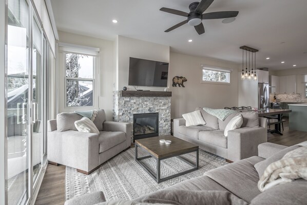 A modern living room with two sofas, a coffee table, a fireplace, and a TV mounted on the wall.
