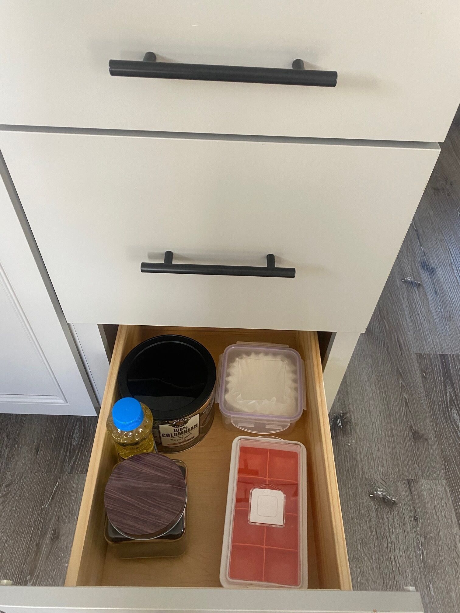 A drawer with a black handle, containing a jar labeled '100% Colombian', a purple container, a red container, and a brown container.
