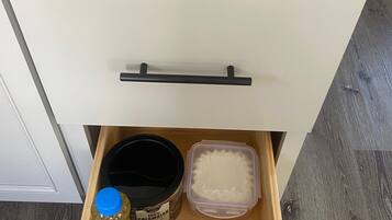 A drawer with a black handle, containing a jar labeled '100% Colombian', a purple container, a red container, and a brown container.