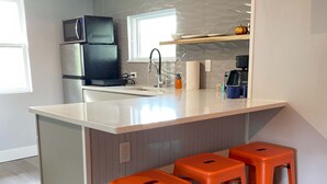 A modern kitchen with a central island, stainless steel appliances, and orange stools. - The Contemporary (Sanford)