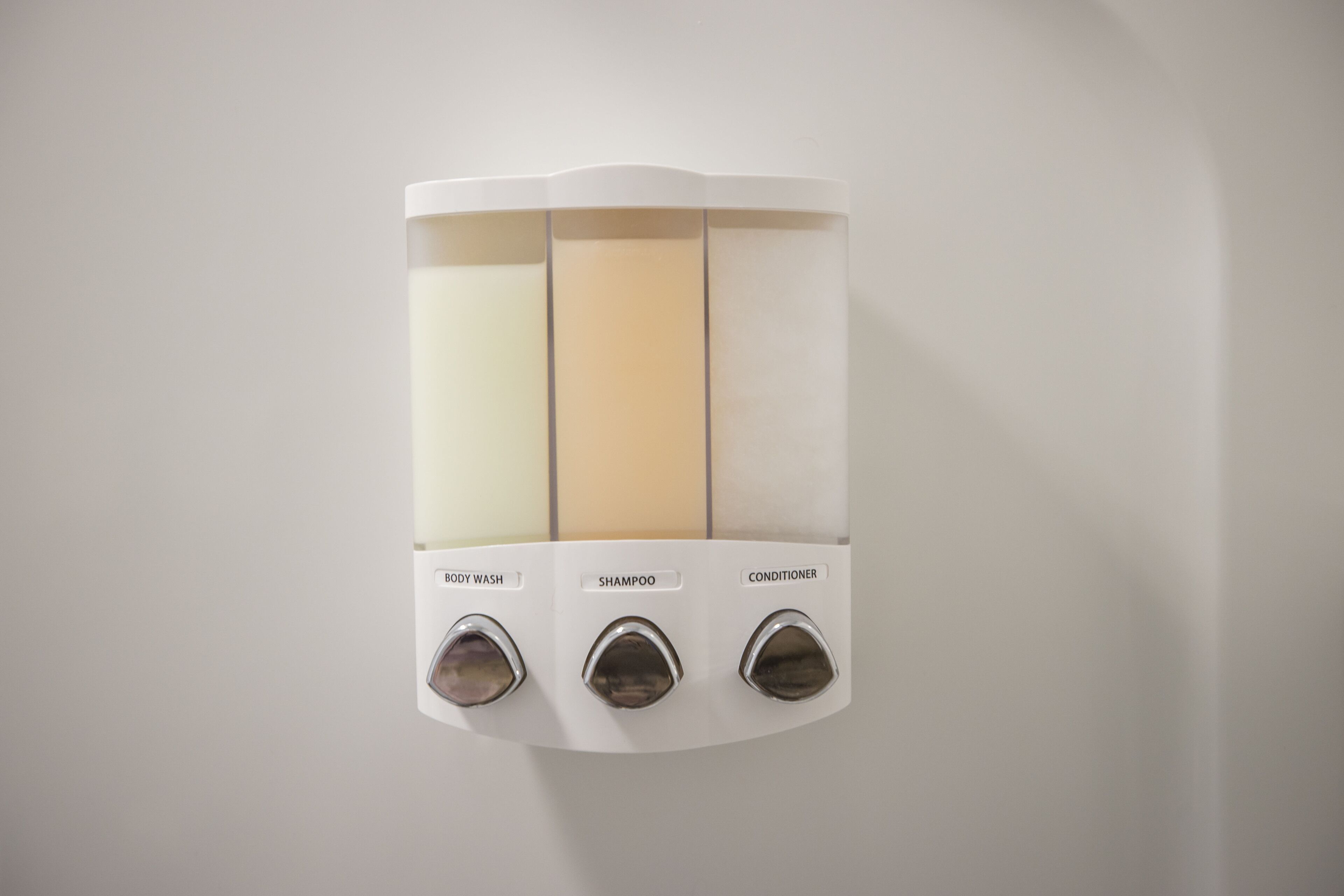 A wall-mounted dispenser with three compartments labeled body wash, shampoo, and conditioner.