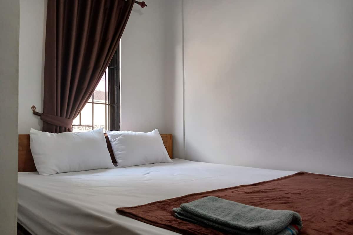 A neatly made bed with white linens, a brown blanket, and two pillows.