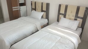 A room with two single beds, each with a wooden headboard and white bedding.