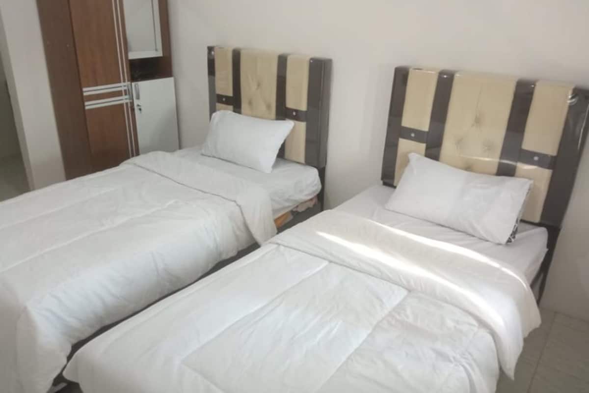 A room with two single beds, each with a wooden headboard and white bedding.