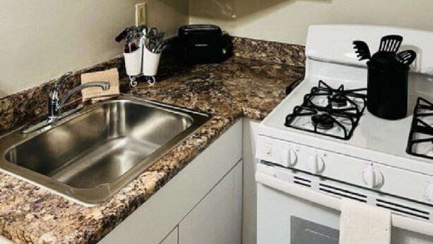 A kitchen with white cabinets, a granite countertop, a stainless steel sink, and a gas stove. - Corporate Rental Apartment In Northwest Indiana (Lake Station)