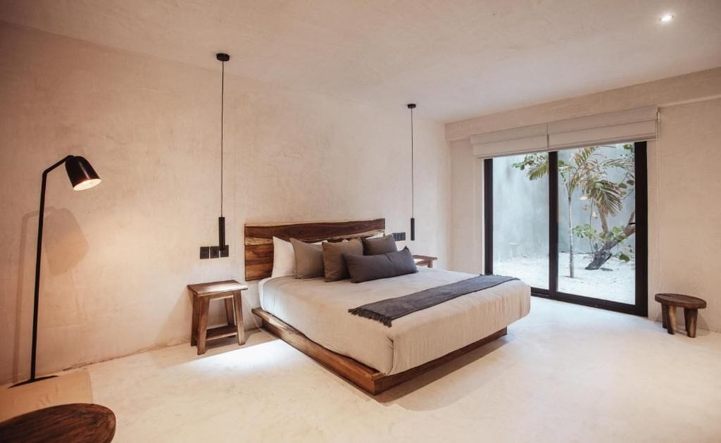 Une chambre moderne avec un grand lit, des tables de chevet, une lampe sur pied et une vue sur l’extérieur grâce à une porte coulissante.