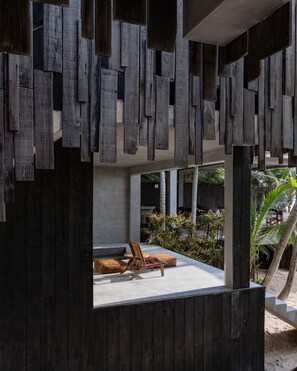 A modern outdoor seating area with a concrete floor and wooden furniture, surrounded by a wooden structure with vertical slats.