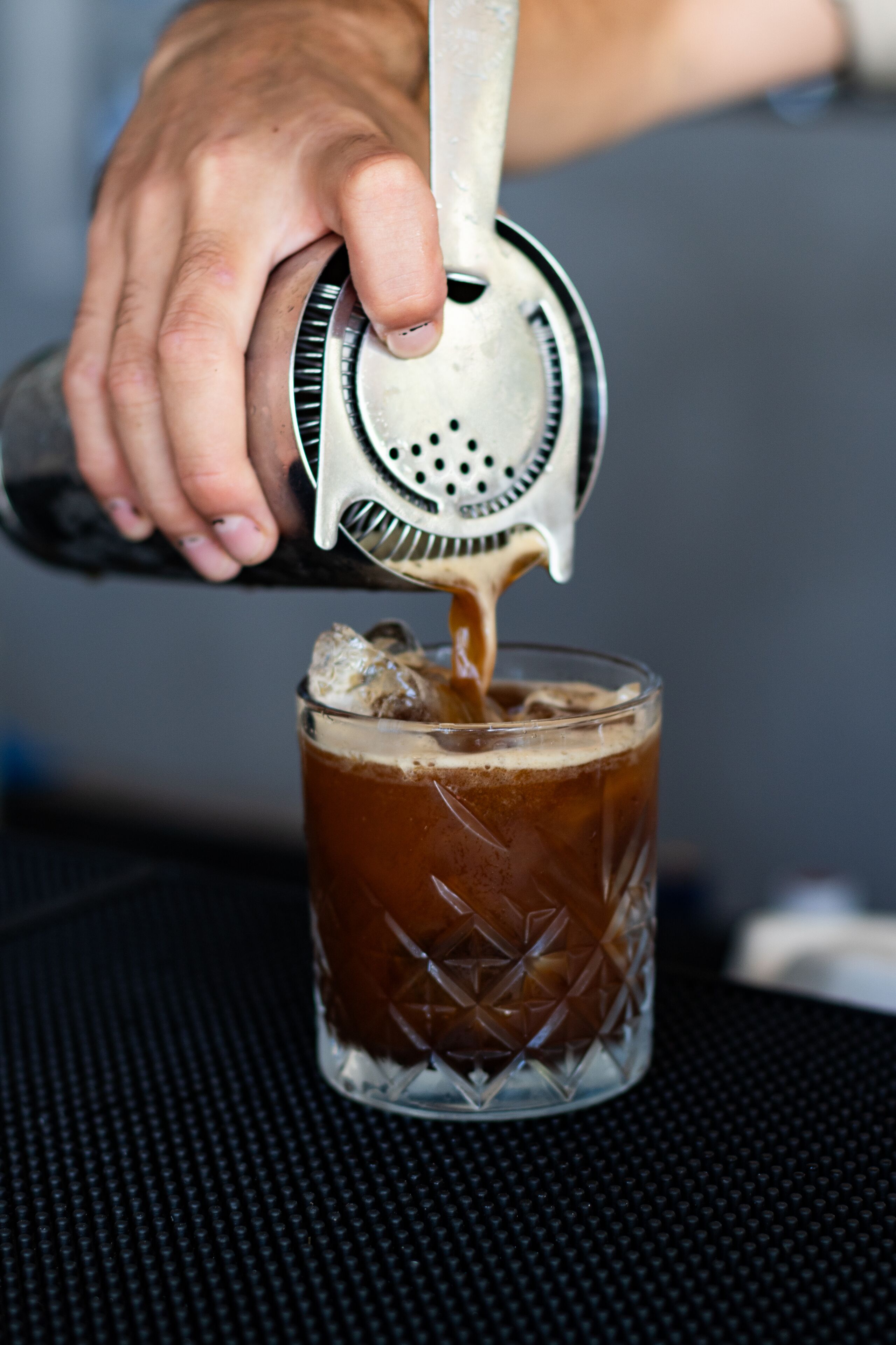 Una mano exprimiendo un cítrico con un exprimidor metálico en un vaso con hielo, probablemente preparando un cóctel.