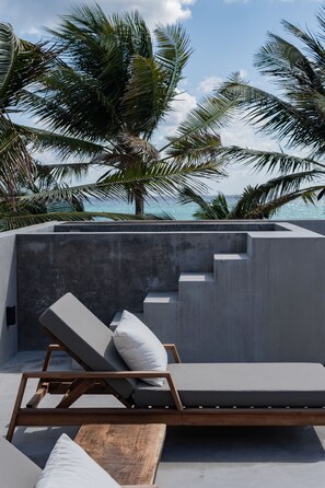 A modern outdoor lounge area with a concrete wall, a wooden bench, and a lounge chair with cushions.