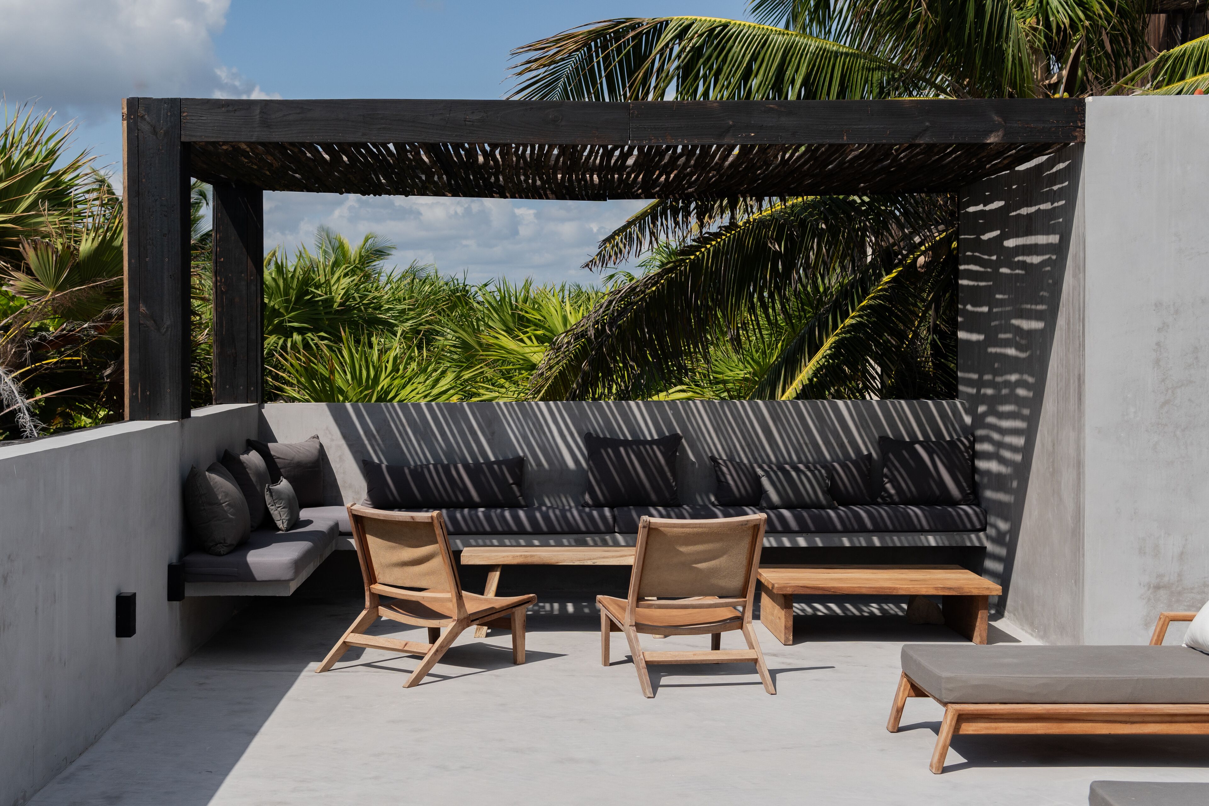A modern outdoor seating area with a wooden bench, two chairs, and a sofa with cushions.