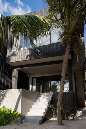 A modern building with a concrete staircase leading to a balcony, surrounded by palm trees and plants.