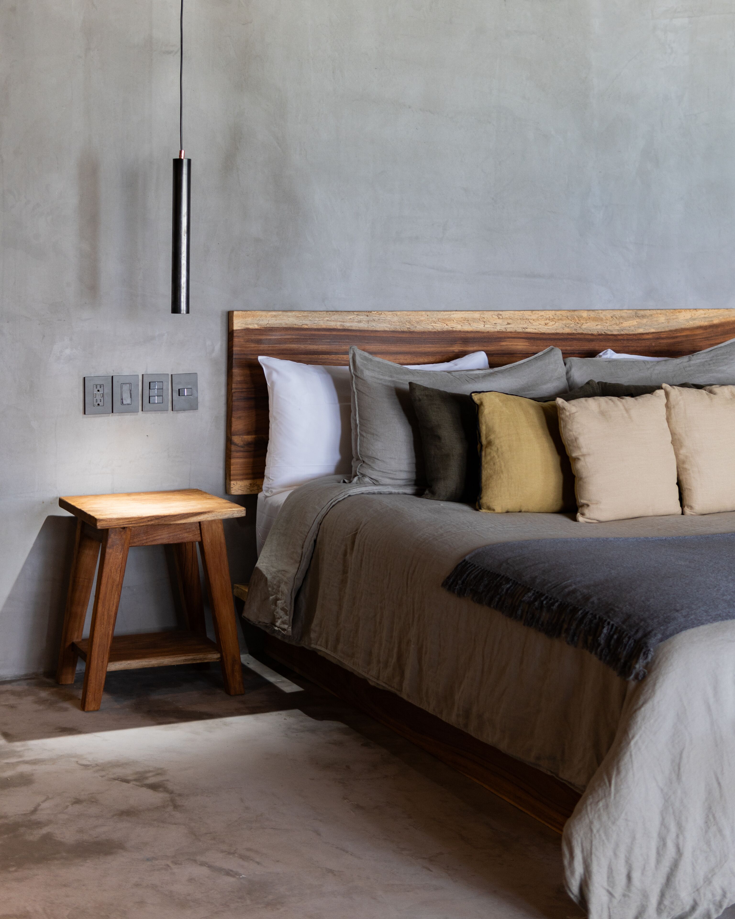 A bedroom with a wooden headboard, a bedside table, and a bed with multiple pillows.