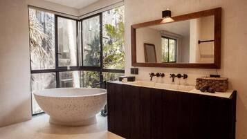 Un baño moderno con una bañera independiente, un espejo grande y una ventana con vistas a palmeras.