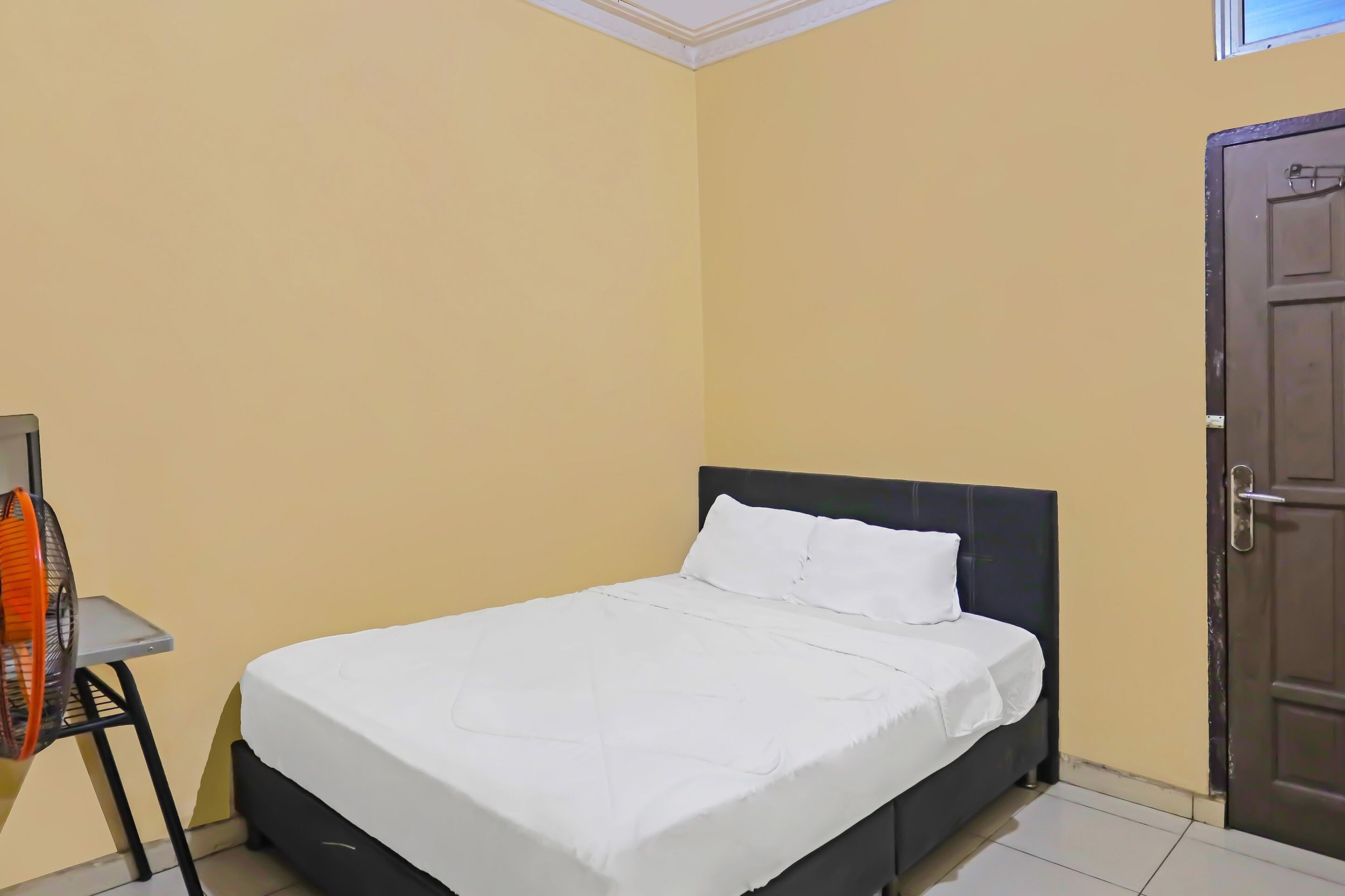 A neatly made bed with white bedding in a room with yellow walls and a dark wooden door.