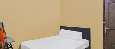 A neatly made bed with white bedding in a room with yellow walls and a dark wooden door.