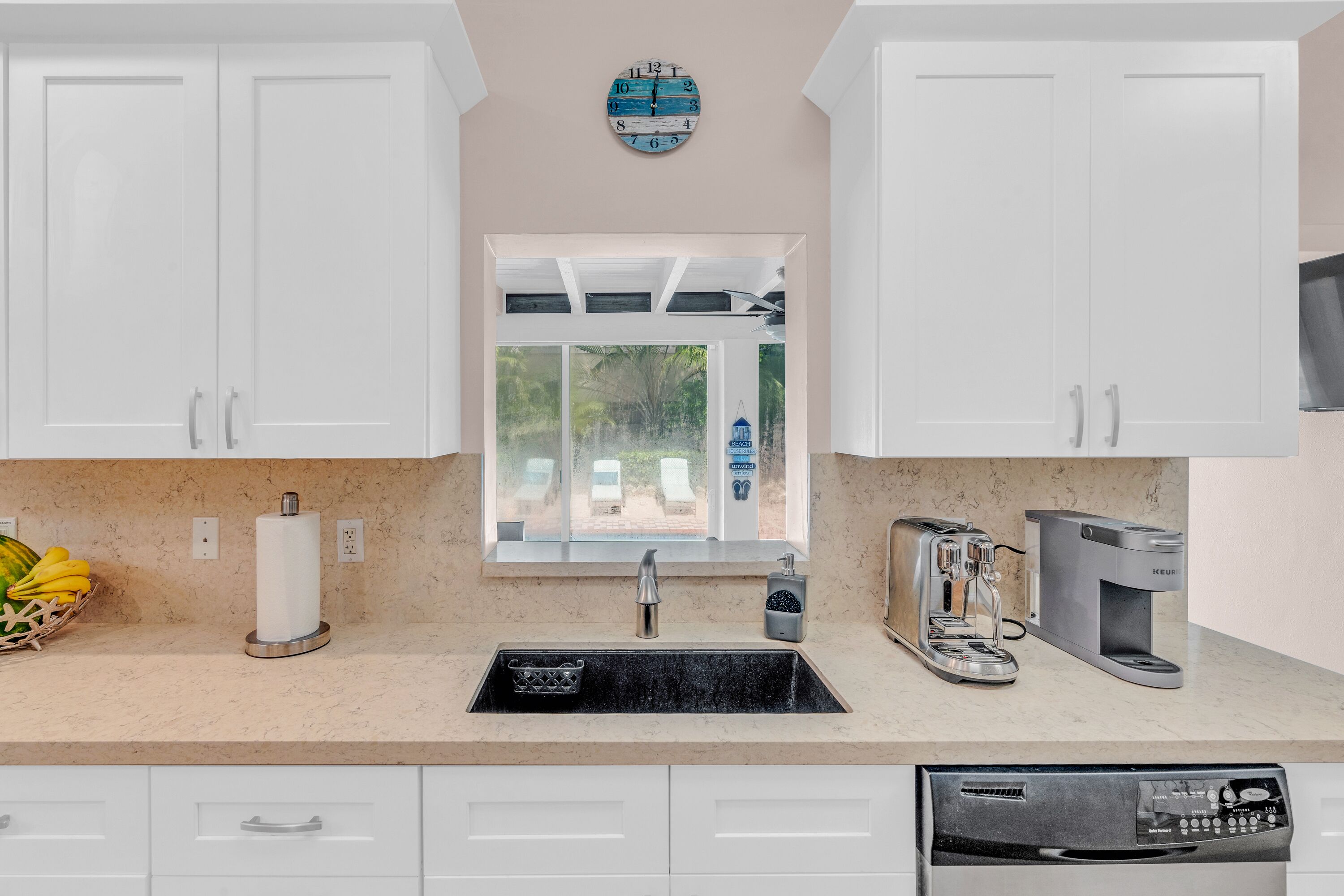 A kitchen with white cabinets, a window, a sink, a toaster, a coffee maker, and a dishwasher.