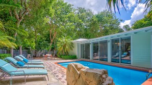 Un jardin avec une piscine, des chaises longues et un petit bâtiment doté de grandes fenêtres.