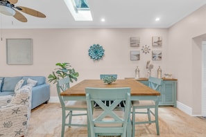 A dining area with a wooden table and teal chairs, a ceiling fan, and wall art.