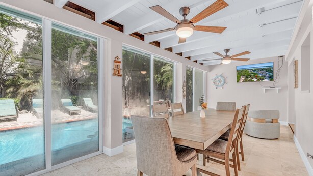 Un vaste espace dédié à la salle à manger, avec une grande table en bois, des chaises confortables et une vue sur une piscine, visible à travers de grandes portes vitrées.