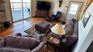 A spacious living room with a high ceiling, wooden flooring, a fireplace, a television, and a sliding glass door leading to an outdoor area. - Gorgeous Lake View with Pontoon!

 (Park Rapids)