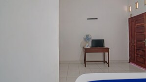A room with a bed, a wooden table with a fan, and a wardrobe. - SPOT ON 92498 Fanni Homestay (Pekanbaru)