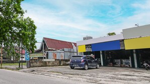 A parking area with a blue car, a building with a yellow and blue facade, and a signboard. - SPOT ON 92498 Fanni Homestay (Pekanbaru)