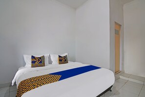 A neatly made bed with a blue and yellow patterned bedspread and pillows, a white wall, and a door leading to another room. - SPOT ON 92498 Fanni Homestay (Pekanbaru)