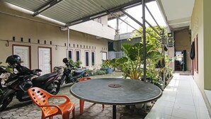 A covered outdoor area with a table and chairs, potted plants, and parked motorcycles. - SPOT ON 92498 Fanni Homestay (Pekanbaru)