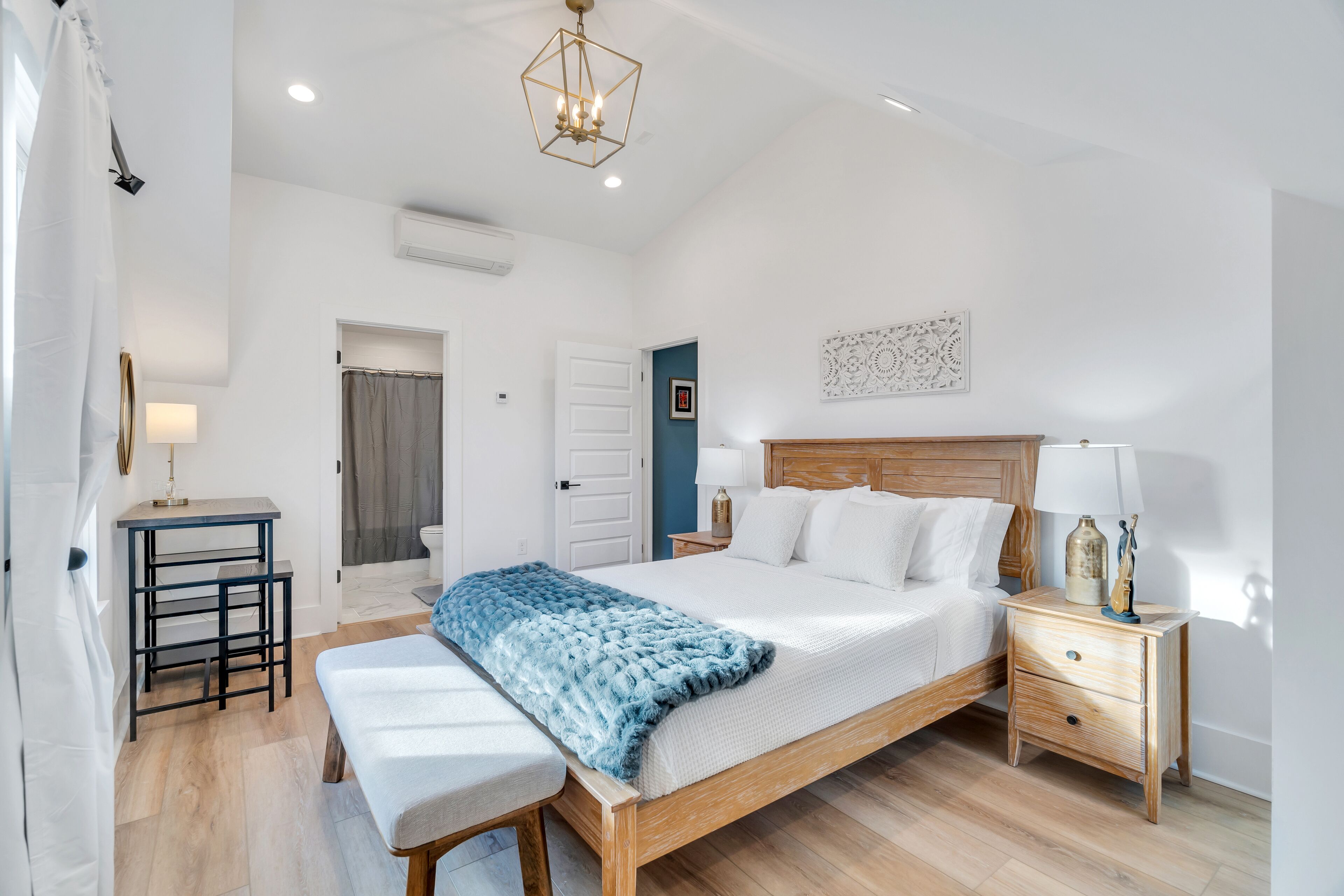 A bedroom with a bed, bedside tables, a bench, and a hanging light fixture.