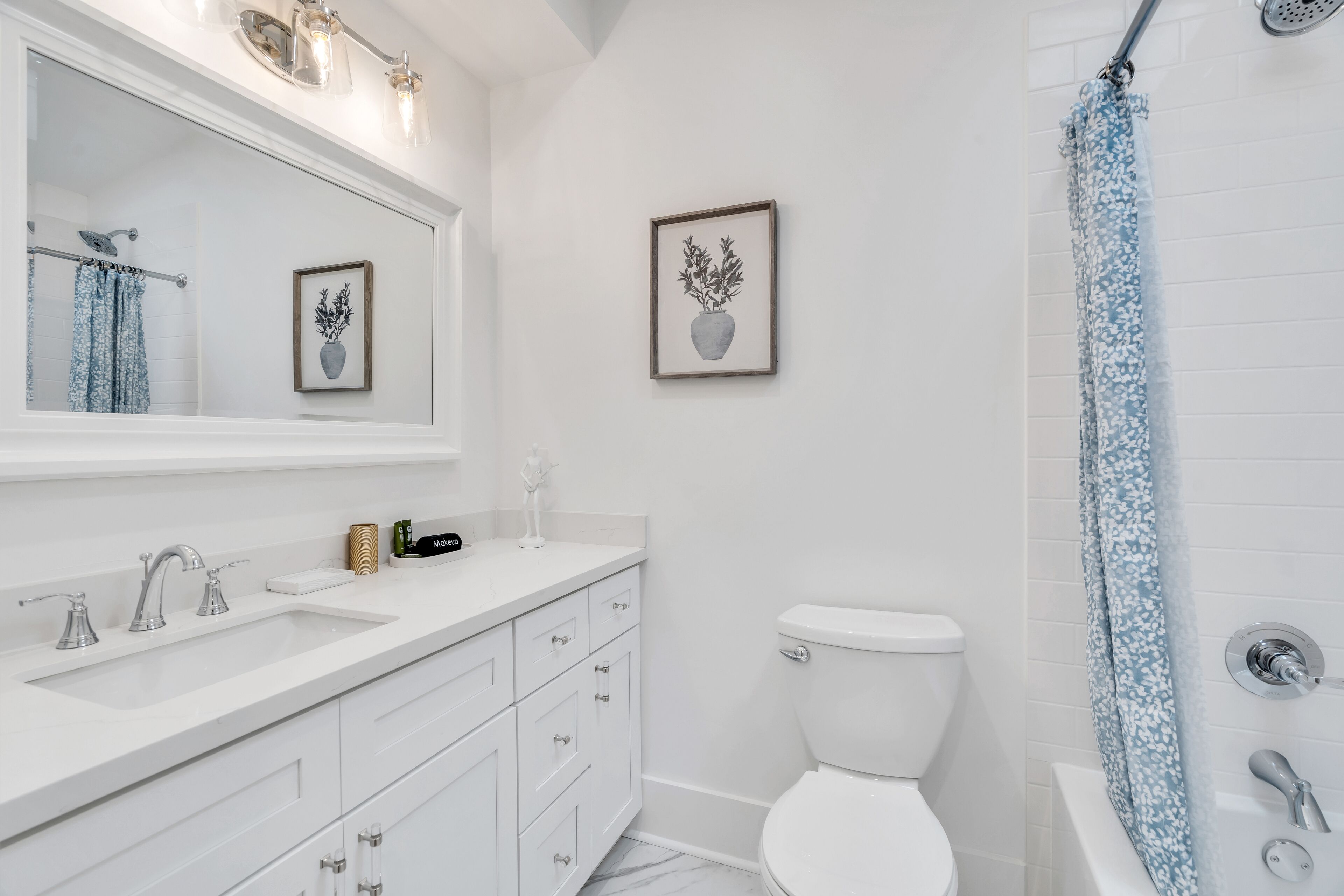 A modern bathroom with a white sink, vanity, and toilet. There is a shower with a floral curtain.