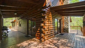 A log cabin with a deck, a stone wall, and a grill area.