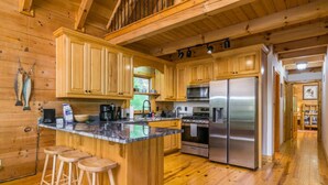 A wooden cabin-style kitchen with a central island, wooden bar stools, a stainless steel refrigerator, and a stove.