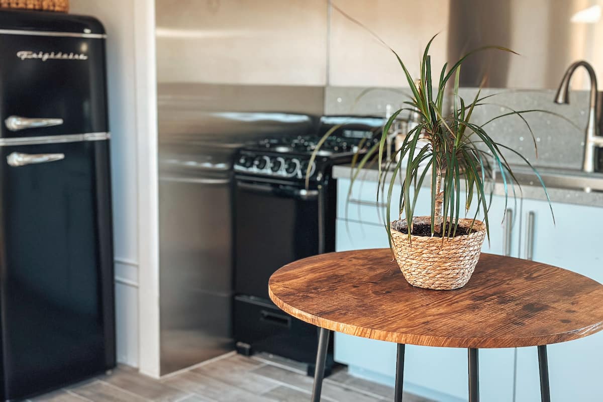 A kitchen with a black refrigerator, a stove, and a round wooden table with a woven basket containing a plant.