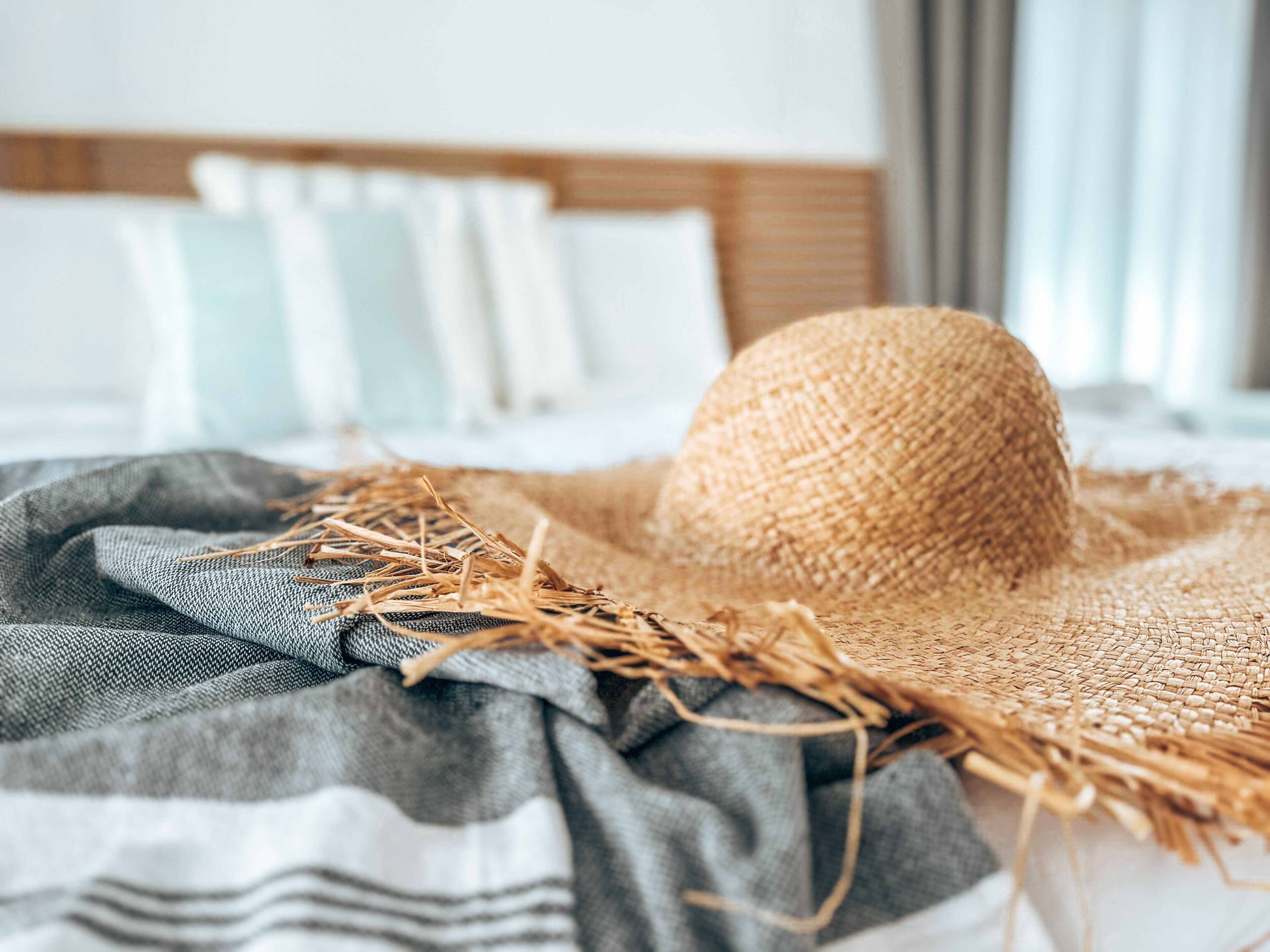 A straw hat on a bed with a striped blanket.