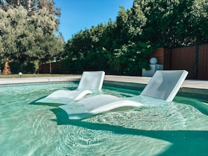 Una piscina al aire libre, sombrillas, sillones reclinables de piscina