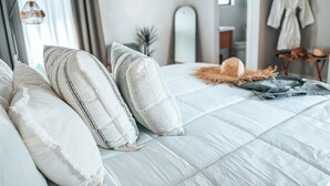 Ein ordentlich bezogenes Bett mit weißer Bettwäsche und gestreiften Kissen, ein Spiegel an der Wand und ein Bademantel auf einem Wäscheständer.