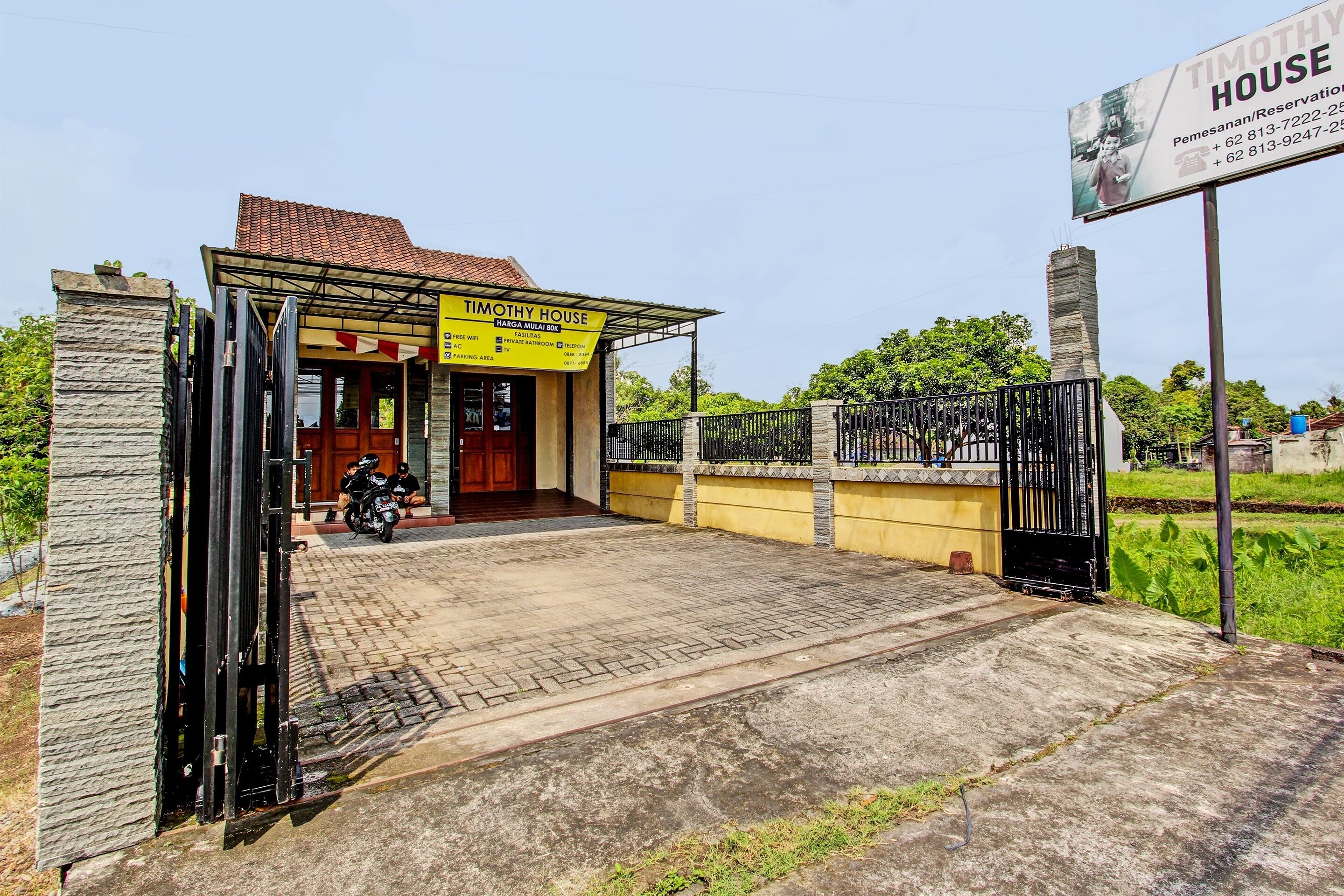 A house with a yellow signboard, a gated entrance, and a motorcycle parked outside.