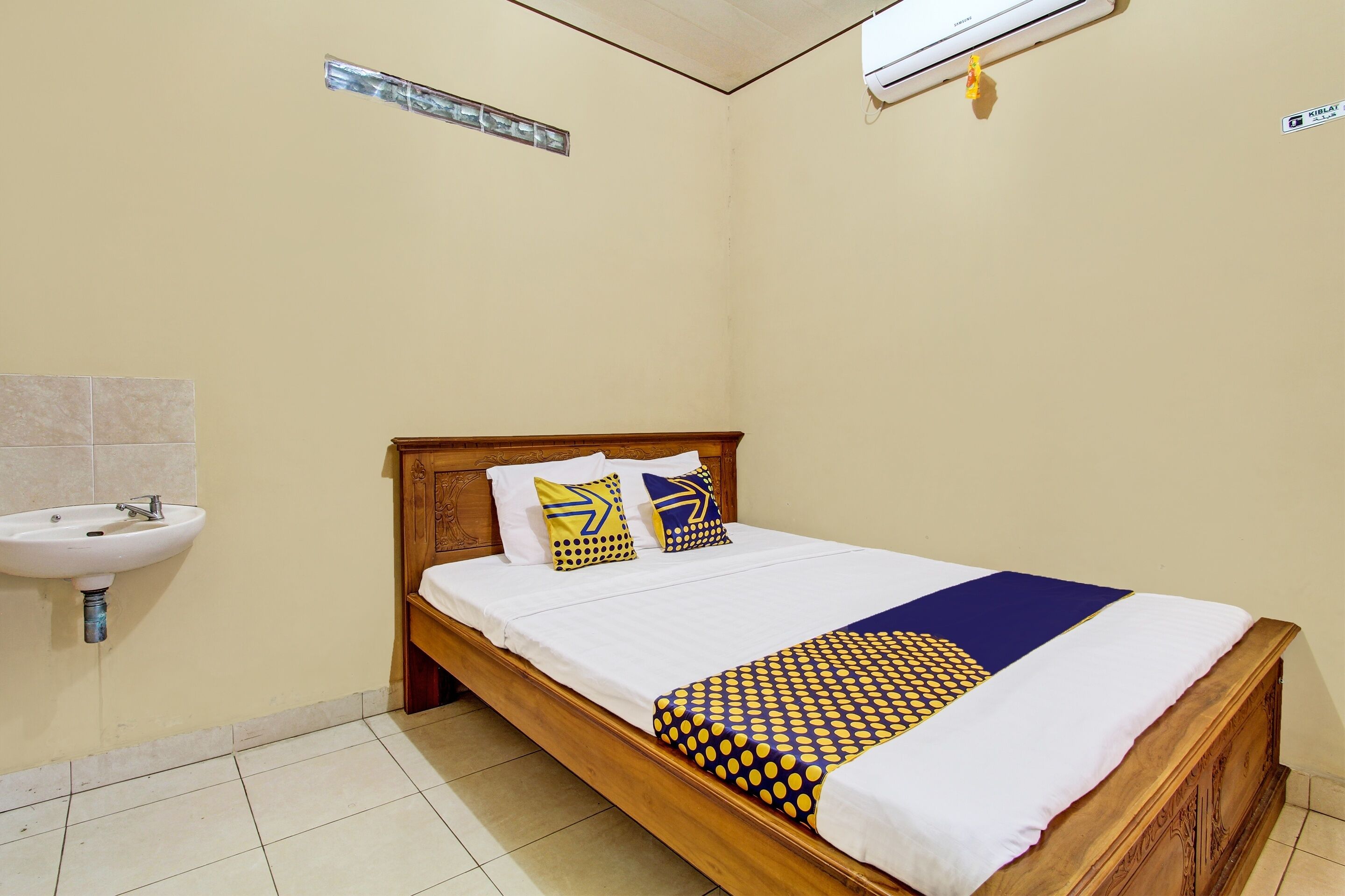 A bedroom with a wooden bed, white bedding, and a blue and yellow patterned blanket.