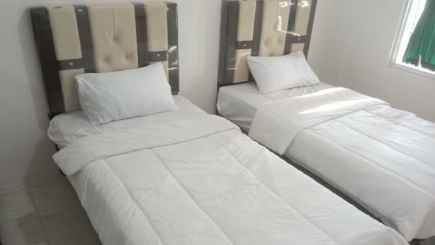 Dos camas individuales con ropa blanca en una habitación con piso de baldosas y ventana con cortina verde.