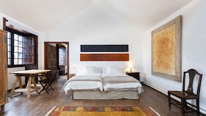 Une chambre avec un plancher en bois, un lit recouvert de draps blancs, un bureau et une chaise.