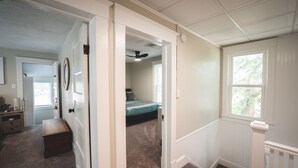 A hallway with a carpeted floor, a wooden bench, a door, and a window with a view of greenery outside.