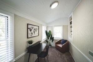 Quarto com escrivaninha, cadeira, planta grande e sofá de couro marrom.