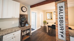 A kitchen with white cabinets, a clock, a coffee station, and a brick accent wall with 'SALISBURY' written on it.