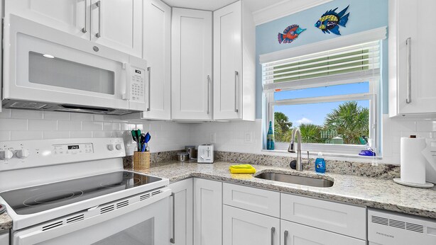 A modern kitchen with white cabinetry, a built-in microwave, a stove, and a window with a view of palm trees. - Surfs Up - 1 Block to Beach & Walk to Dining (Flagler Beach)