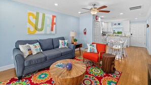 A living room with a grey sofa, a red armchair, a wooden coffee table, and a colorful rug. - Surfs Up - 1 Block to Beach & Walk to Dining (Flagler Beach)