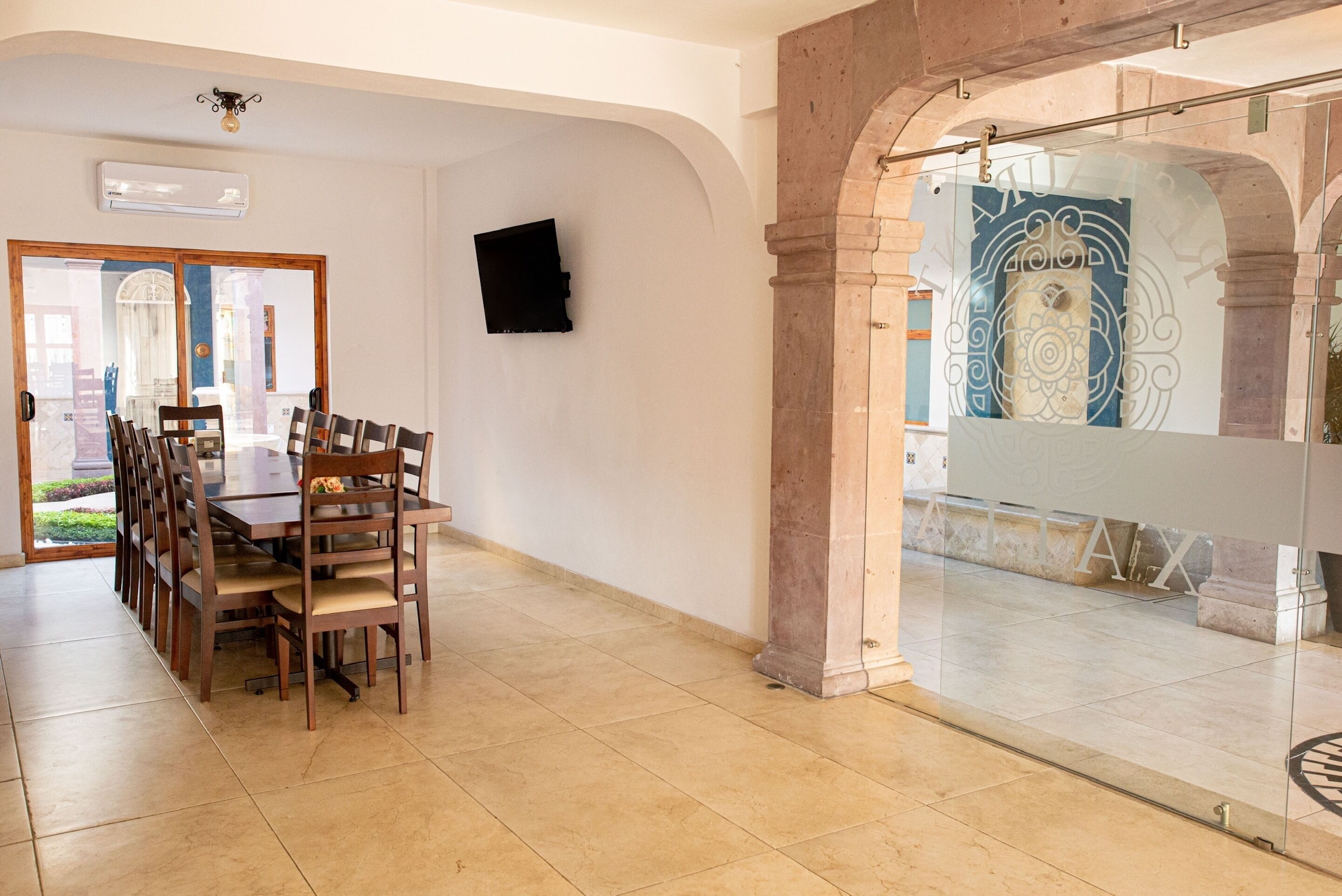 A dining area with a wooden table and chairs, a wall-mounted TV, and a glass partition with a decorative design.