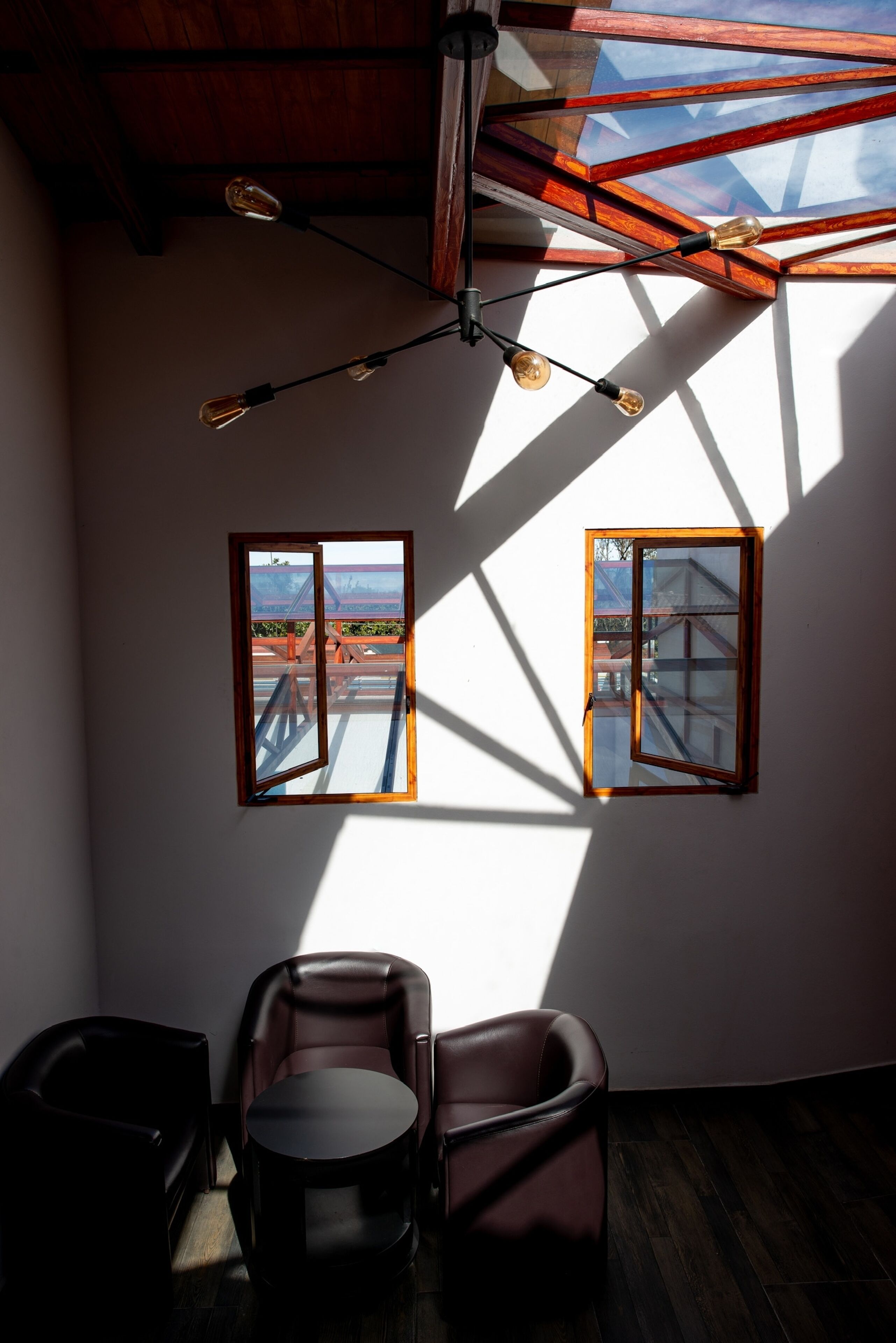 Una habitación con dos ventanas, un candelabro en el techo y una mesa redonda.