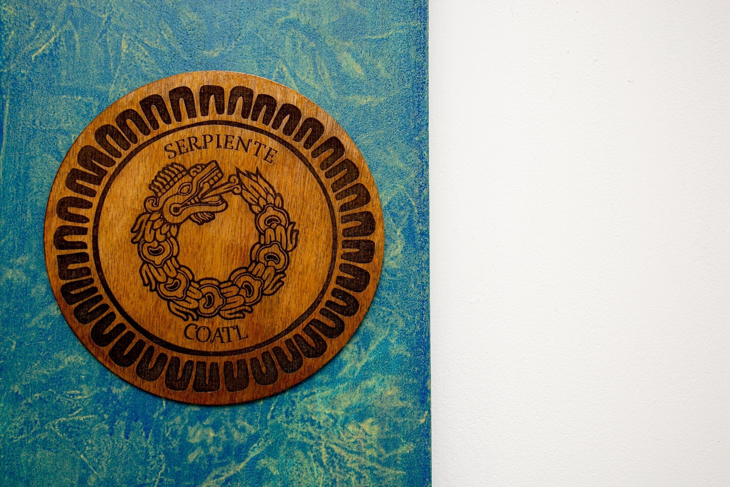 A circular wooden plaque with the text "SERPENTE" and "COATI" engraved on it.